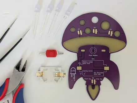 The mushroom-shaped circuit board of the kit, with LEDs, switch and pliers laid out beside it