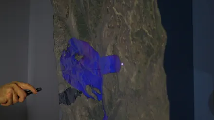 A hand with a laser pointer; simulated blue water spreads across the printed terrain